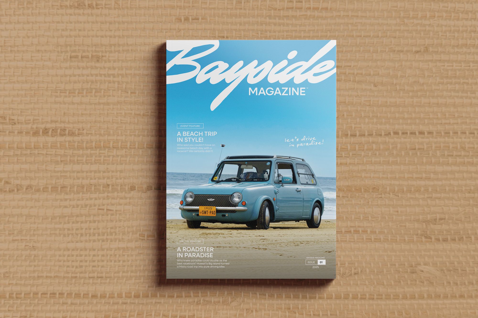 A magazine titled 'Bayside Magazine' standing upright on a textured beige surface. The cover features a vintage blue Nissan Pao parked on a beach under a bright blue sky.
