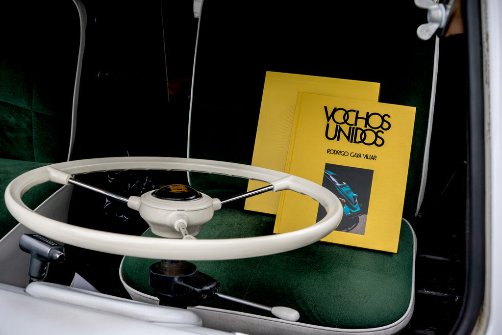 Image of the book Vochos Unidos on the green fabric seat of a Volkswagen Bus in Los Angeles, from the release party for Vochos Unidos by Rodrigo Gaya Villar, published by Carrara Media. A coffee table book of automotive photography showing the Volkswagen Beetle across Mexico, aka "El Vocho." Available now.