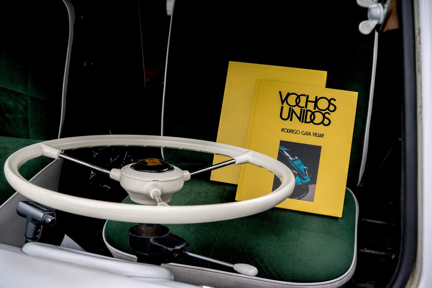 Image of the book Vochos Unidos on the green fabric seat of a Volkswagen Bus in Los Angeles, from the release party for Vochos Unidos by Rodrigo Gaya Villar, published by Carrara Media. A coffee table book of automotive photography showing the Volkswagen Beetle across Mexico, aka "El Vocho." Available now.