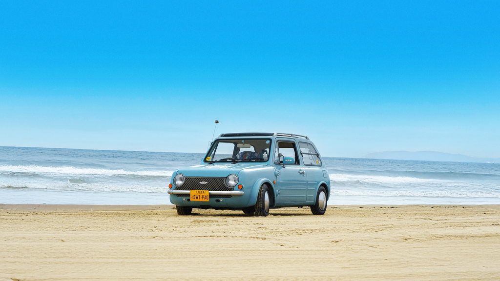 A classic blue Nissan Pao parked on the beach in Southern California, in an image from Bayside Magazine Issue 01, a new periodical celebrating coastal car culture. Published by Carrara Media.