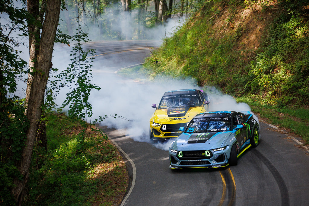 Image of Vaughn Gittin Jr. and Chelsea DeNofa driving two Ford Mustang RTR FD drift cars on a mountain road, photo by Larry Chen. From the new book Ready To Rock by Vaughn Gittin Jr. with Mike Spinelli, foreword by T-Pain, published by Carrara Media. The story of RTR Vehicles and professional drifting, off-road racing and the Ford RTR Mustang and RTR Bronco.