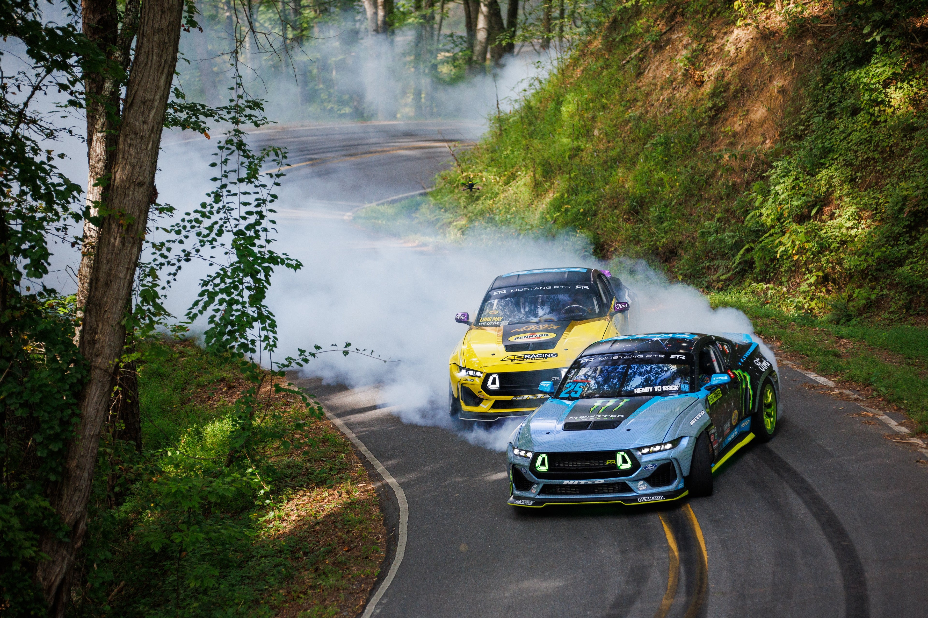 Image of Vaughn Gittin Jr. and Chelsea DeNofa driving two Ford Mustang RTR FD drift cars on a mountain road, photo by Larry Chen. From the new book Ready To Rock by Vaughn Gittin Jr. with Mike Spinelli, foreword by T-Pain, published by Carrara Media. The story of RTR Vehicles and professional drifting, off-road racing and the Ford RTR Mustang and RTR Bronco.